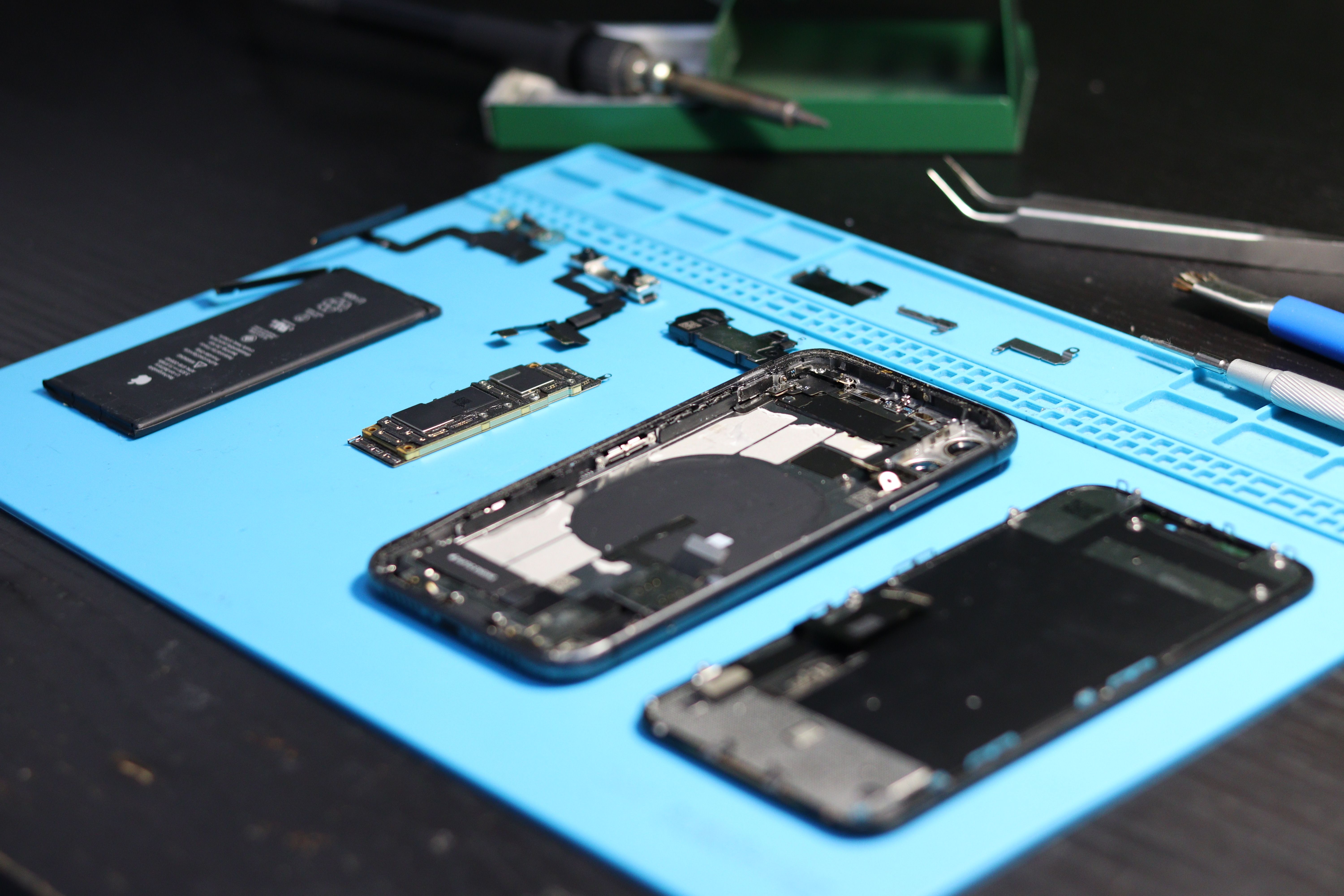 Phone fully disassembled on an anti-static repair mat, with the logic board, battery, and small components laid out for repair